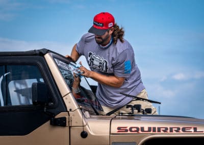 Man applying BF Goodrich decal to upper part of windshield of copper colored Jeep